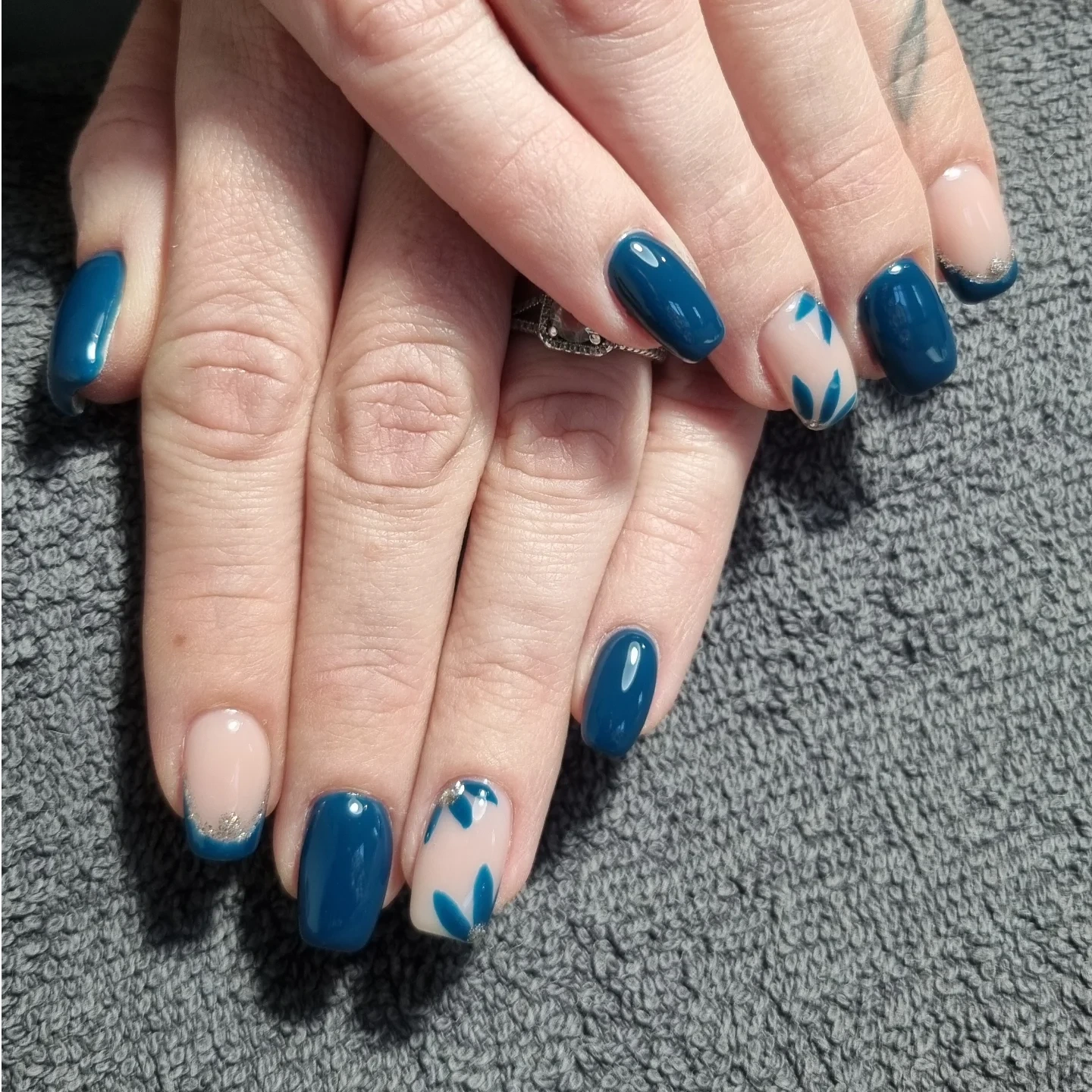 Manucure avec vernis bleu canard et motifs feuillage réalisés au salon de beauté.